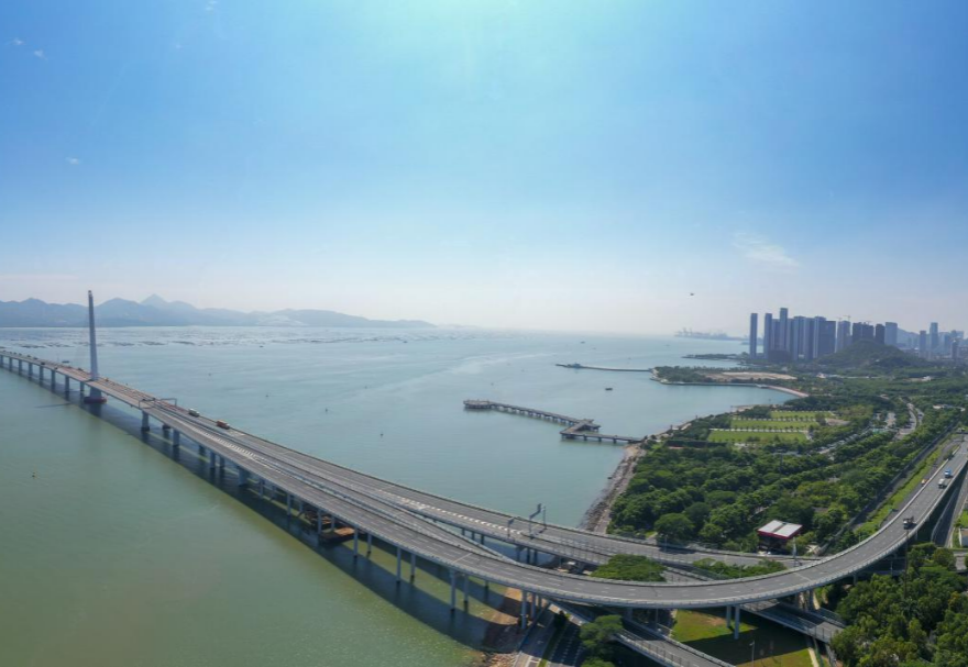 深圳湾大桥是继罗湖、皇岗和沙头角之后深圳第4条跨境通道，全长5545米，设南北两个通航桥，主跨分别为210米和180米。大桥连接深圳蛇口与香港元朗，为中国公路干线网中唯一与香港连接的高速公路大桥，也是广深沿江高速公路的咽喉。广州与香港的距离因该桥建成通车缩短至100千米。大桥深圳侧独塔斜拉桥塔采用向香港侧倾斜的斜塔，与香港侧斜拉桥的桥塔向深圳侧倾斜互相对应，寓意深港两地手牵手走向一起。图为深圳湾大桥。