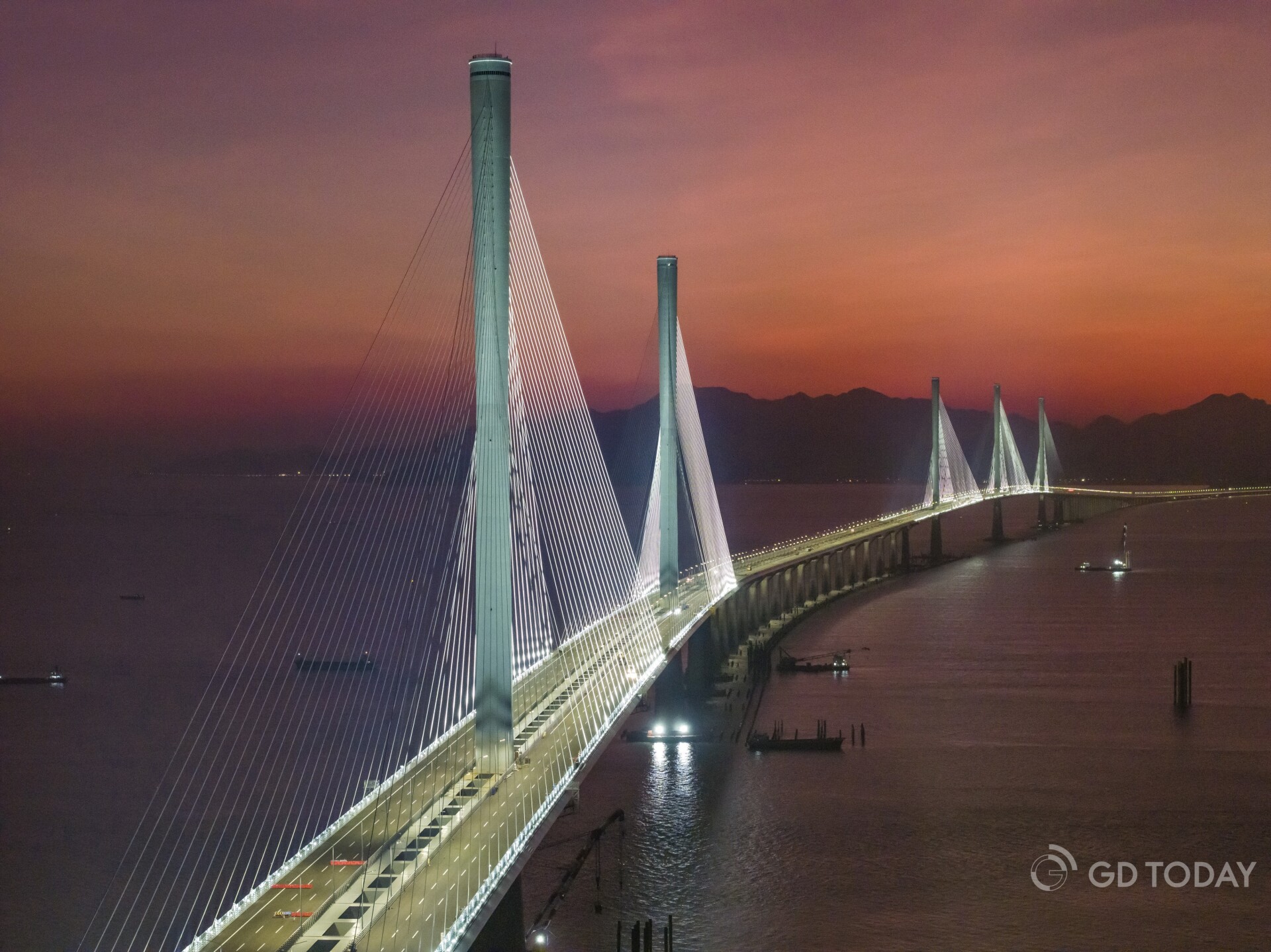 As night falls, the five main towers of the Huangmaohai Passage light up, casting a glow that complements the setting su